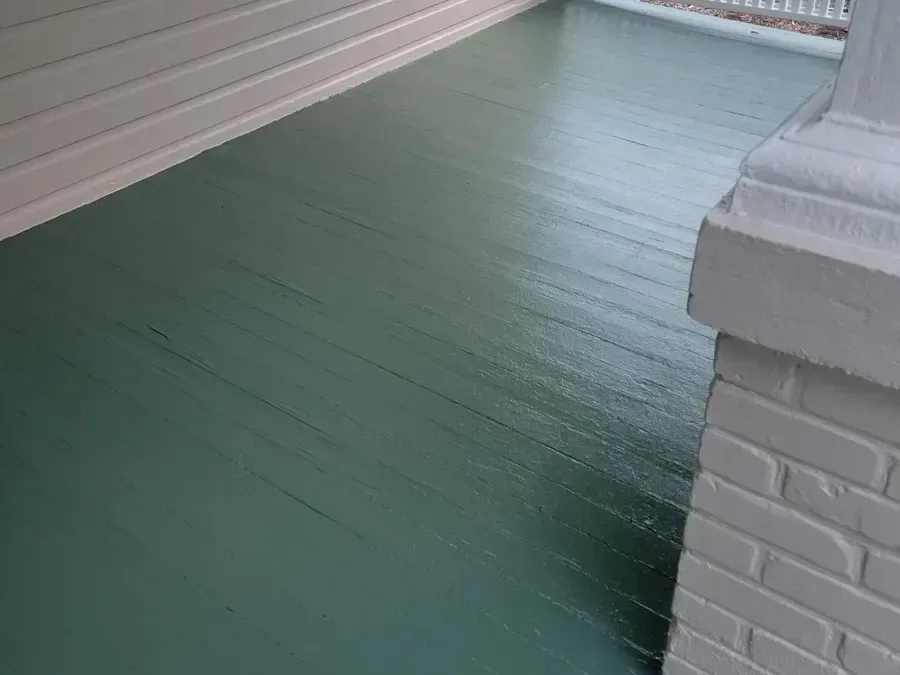 The same porch floor refinished in a glossy heritage green next to freshly painted white brick
